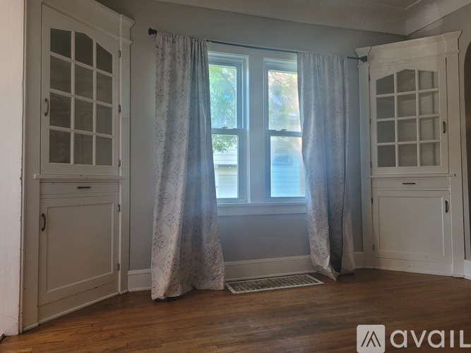 A room with a window, curtains, and a wooden floor.