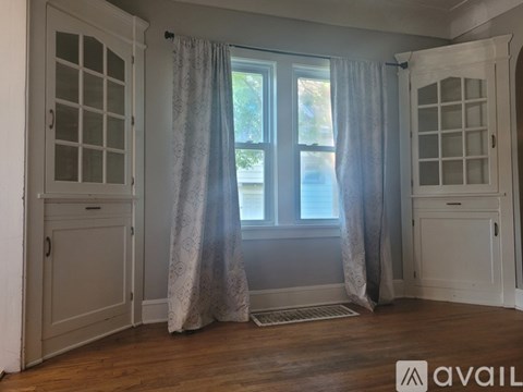 A room with a window, curtains, and a wooden floor.