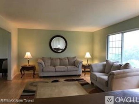 A living room with a grey sofa and a round mirror on the wall.