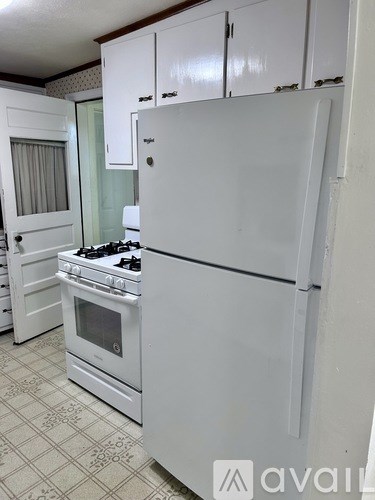 A white refrigerator stands in a kitchen with a white stove and oven.