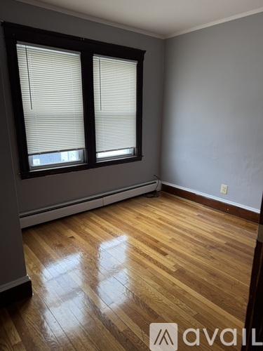 A room with wooden floors and two windows with blinds.