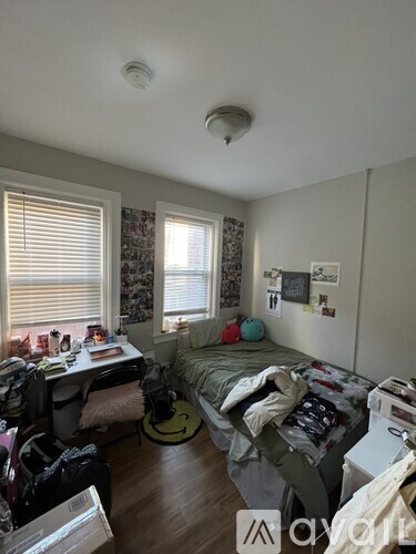 A bedroom with a bed, desk, and window with blinds.
