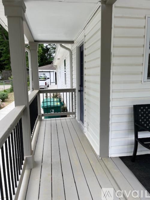 A white porch with a black chair and a white railing.