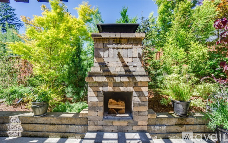 A stone fireplace is surrounded by green plants and trees.