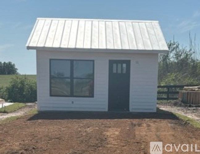 A small white house with a grey door and windows is available for purchase.