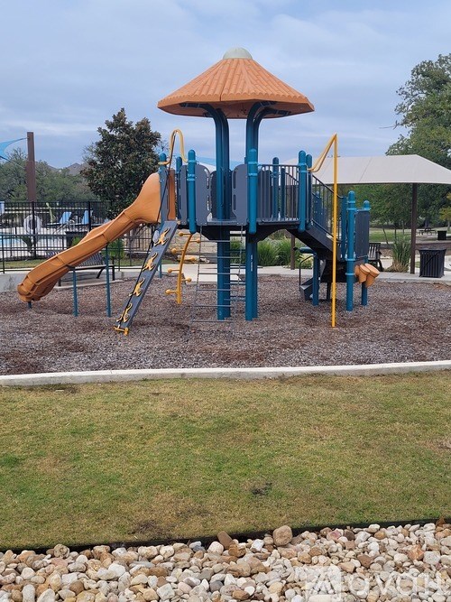 A playground with a blue and yellow slide and a brown roofed structure.