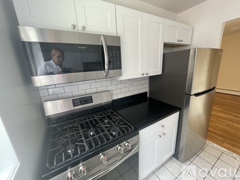 A man is in the kitchen with a stove top oven and a microwave.