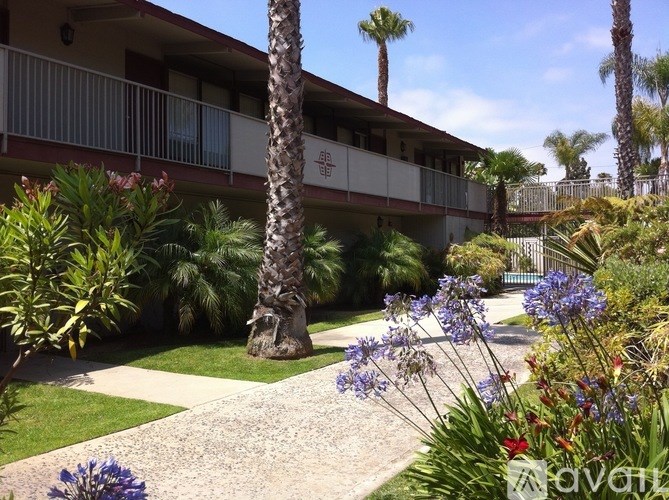 A building with a balcony is surrounded by green plants and trees.