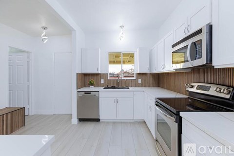 A kitchen with white cabinets and appliances, a window, and a wooden floor.
