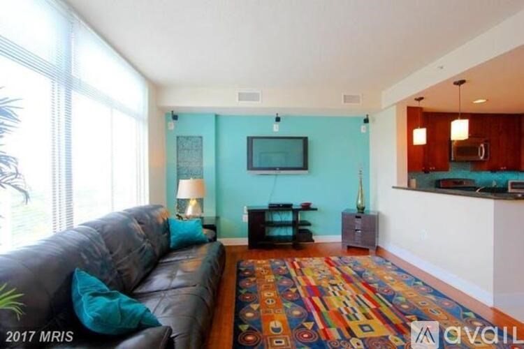 A living room with a black leather couch and a colorful rug.