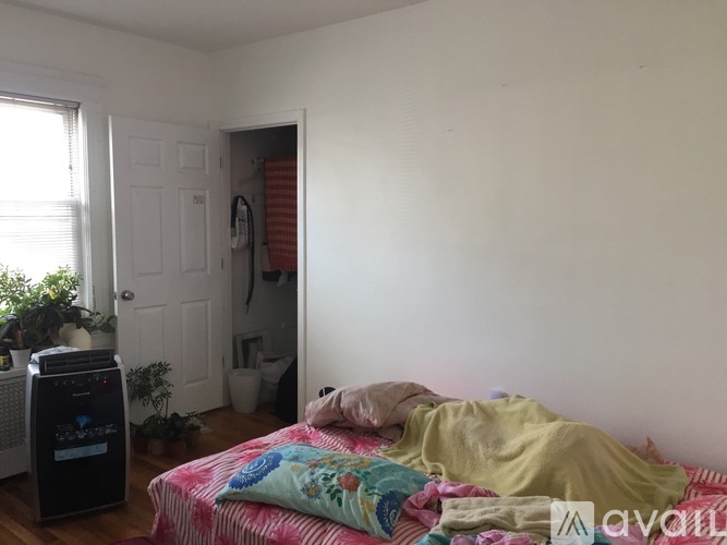 A bedroom with a bed covered in a yellow blanket and a black air purifier on the floor.