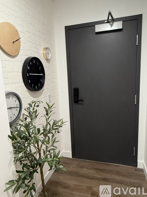 A black door with a silver handle is flanked by two clocks on a white wall.
