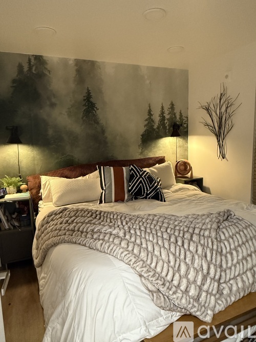 A bedroom with a large bed and a forest mural on the wall.