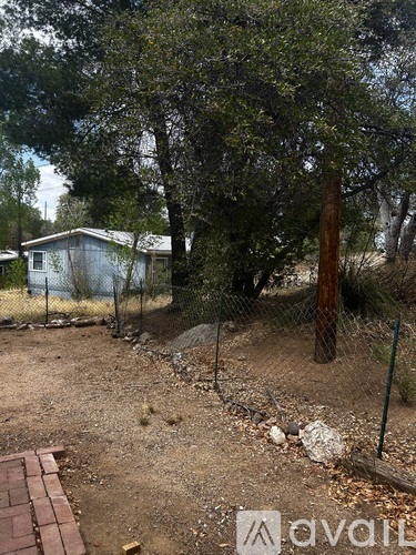A backyard with a fence, a tree, and a small house.