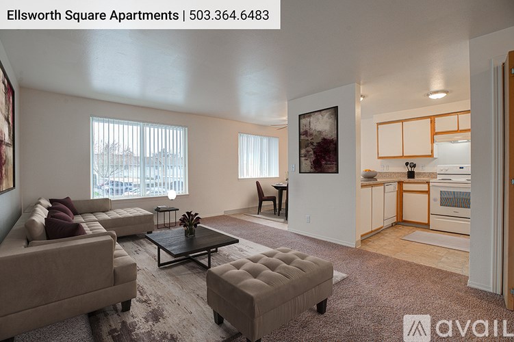 A living room with a couch, coffee table, and a kitchen area in the background.
