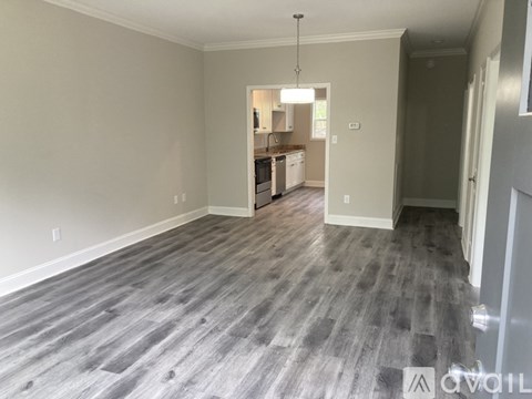 A room with a grey floor and a kitchen in the background.