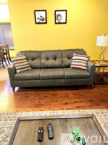 A grey couch with a striped pillow and a coffee table with three remote controls on it.