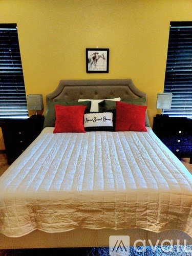 A bed with a white comforter and two red pillows with the name "Jane Doe" on them.