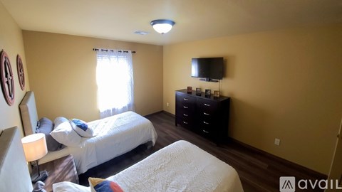 A bedroom with two beds and a dresser with a flat screen TV mounted above it.
