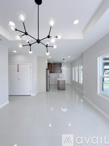 A modern chandelier hangs from the ceiling in a spacious, white-walled room.
