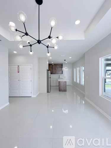 A modern chandelier hangs from the ceiling in a spacious, white-walled room.