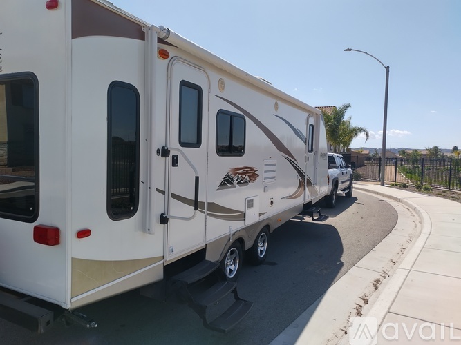 A white RV with a brown stripe is parked on the side of a road.