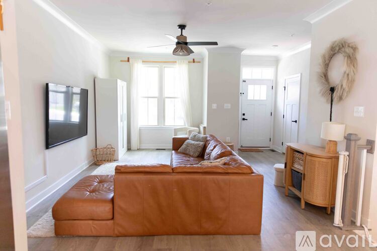 A living room with a brown leather couch and a flat screen TV mounted on the wall.