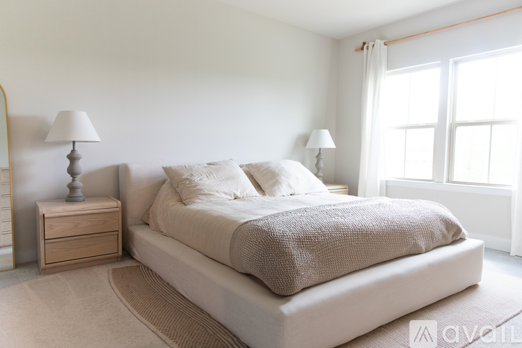 A bedroom with a large bed, a nightstand with a lamp, and a window with curtains.