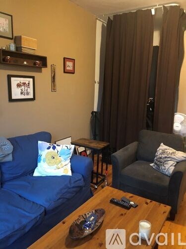 A living room with a blue couch, a grey armchair, a wooden coffee table, and a wall with pictures and a shelf.