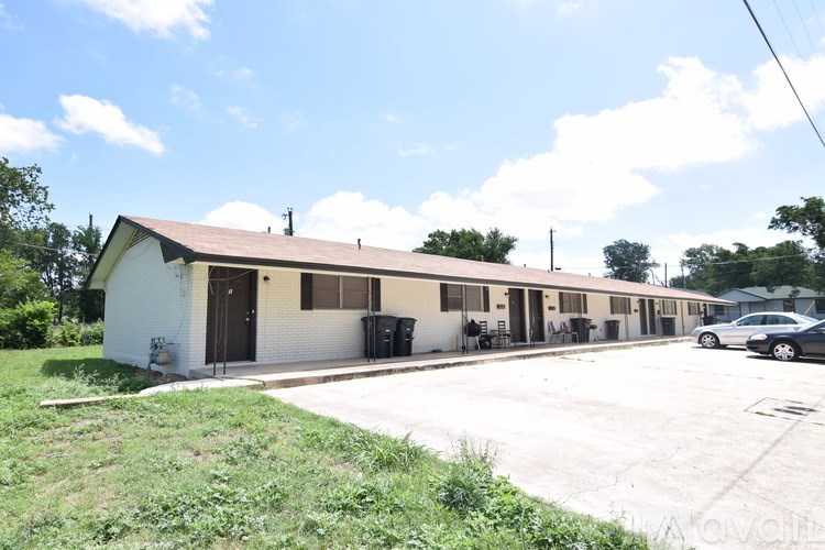 A house with a brown brick exterior is situated on a grassy lot with a road in front.