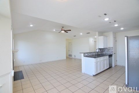 A spacious kitchen and living room with white cabinets and a black countertop.