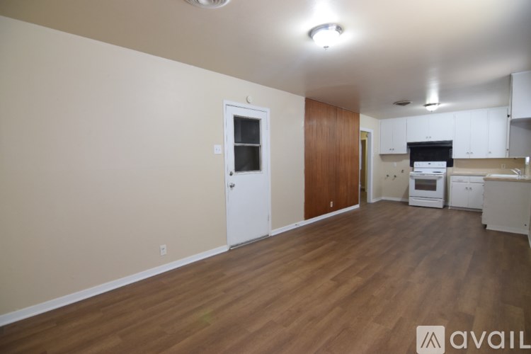 A room with wooden floors and a kitchen area in the background.