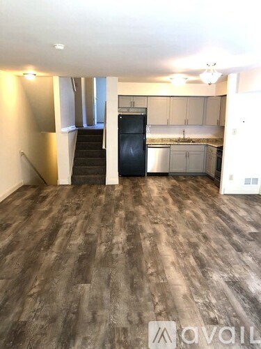 A spacious room with wooden flooring and a staircase leading to another level.