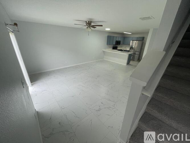 A spacious room with a ceiling fan and a staircase on the right side.