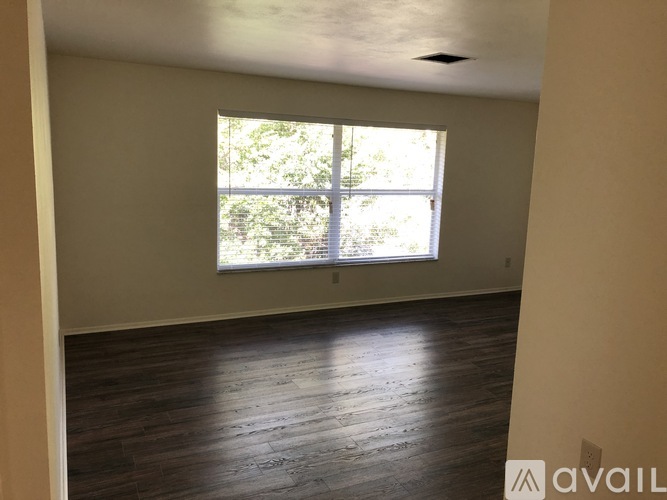A room with wooden flooring and a window showing trees outside.