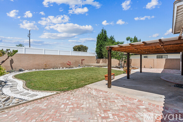 A backyard with a brick walkway and a wooden pergola.