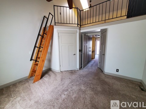 A room with a carpeted floor, a wooden staircase, and a balcony with a metal railing.