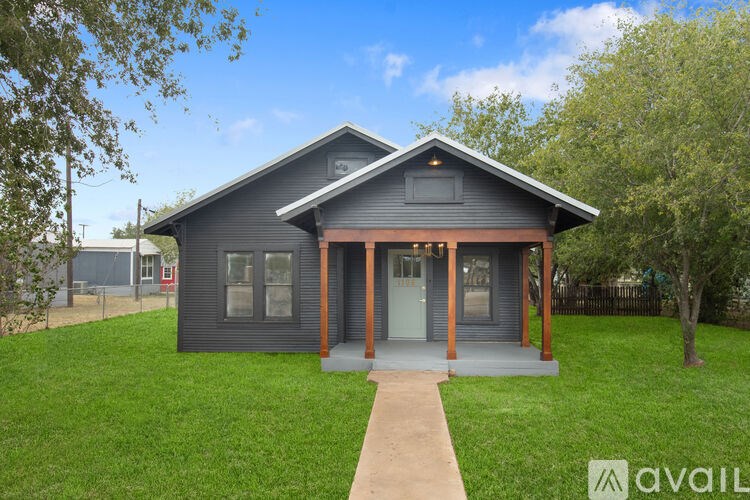 A house with a grey front and a brown door is surrounded by a green lawn.