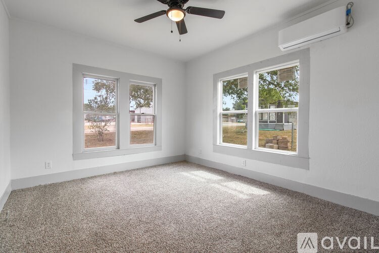 A room with a carpeted floor, a ceiling fan, and two windows with a view of a parking lot.