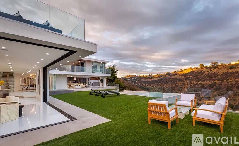 A modern house with a glass balcony and two wooden chairs on the lawn.