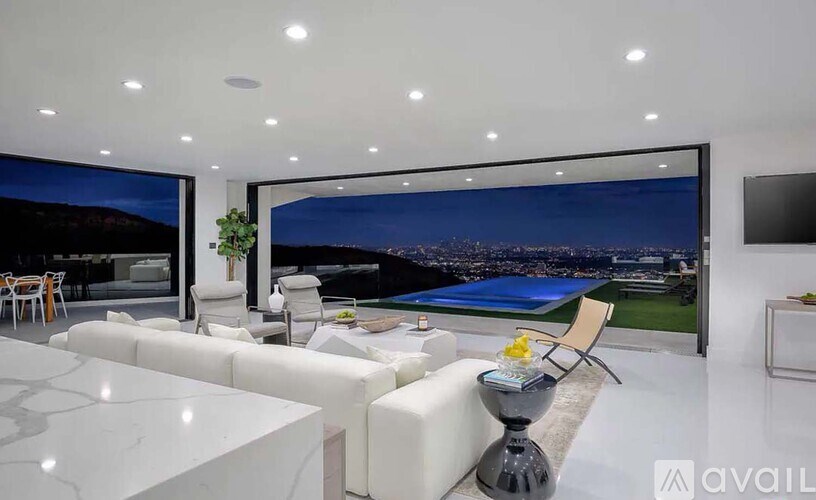 A modern living room with a large window overlooking a cityscape at night.