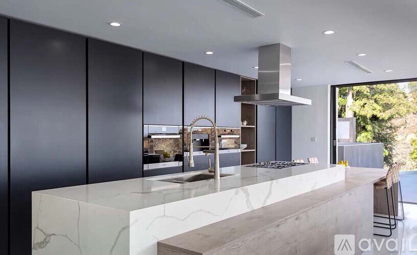 A modern kitchen with a marble countertop and a view of the backyard.
