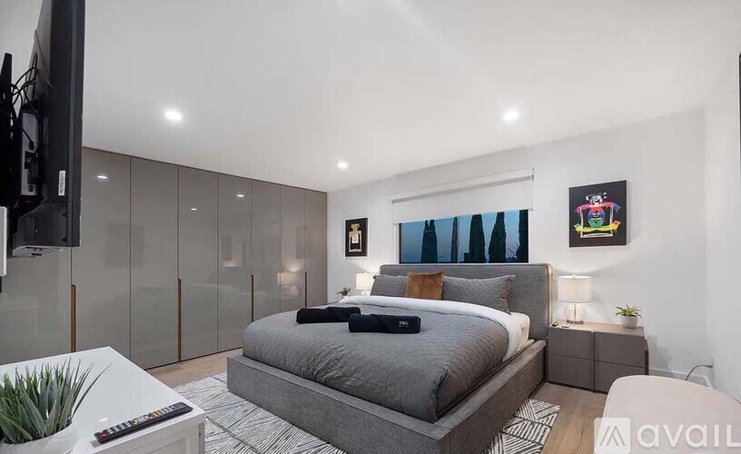 A modern bedroom with a large bed and a flat-screen TV mounted on the wall.
