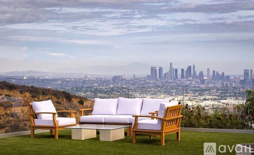Two chairs and a couch are on a lawn with a city skyline in the background.