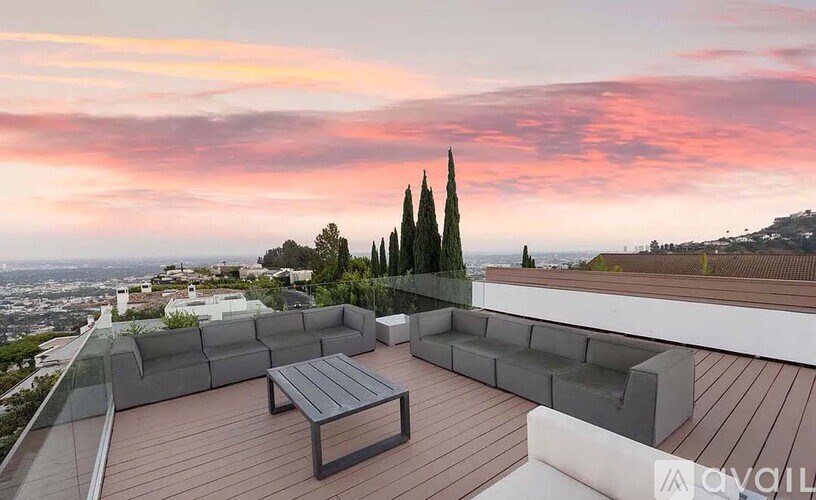 A wooden deck with a bench and a table is set up on a rooftop with a view of the city.