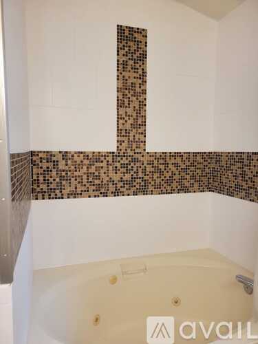 A bathroom with a white tub and brown tiles on the wall.
