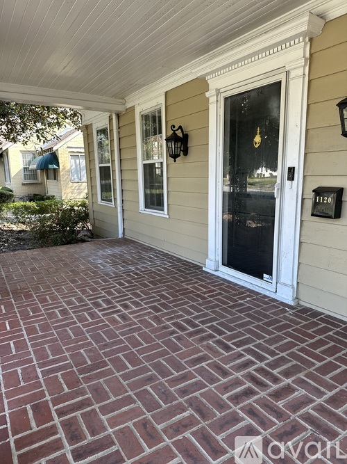 A brick patio leads to a white door with a black window above it.
