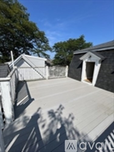 A sunny day at a wooden deck with a white fence and a black building in the background.