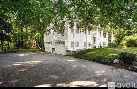 A white house with a driveway and trees surrounding it.