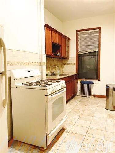 A white gas stove with a white oven is in a kitchen with brown cabinets.